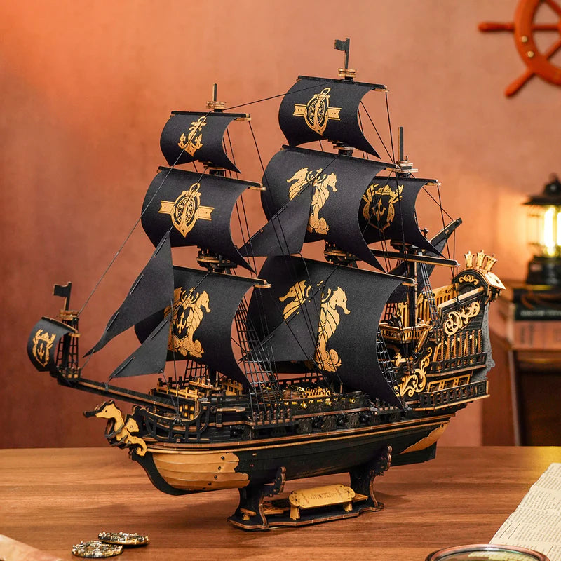 Model of a pirate ship with black sails and gold details on a wooden surface.