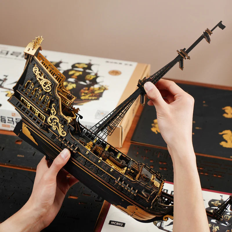 Hand holding a detailed black and gold ship model with a blurred background