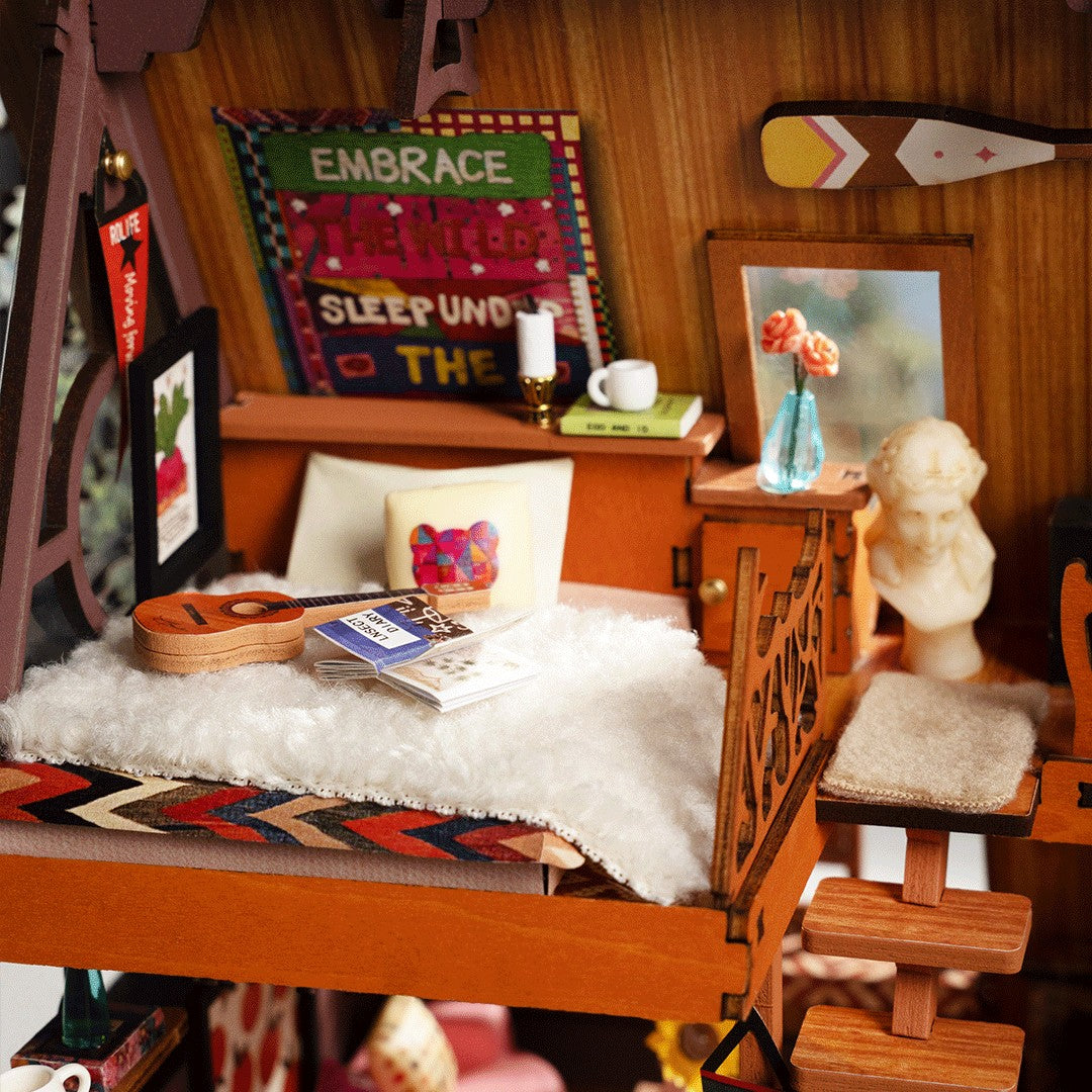 A miniature dollhouse-style bedroom scene with a small wooden bed, white faux-fur bedding, a guitar, framed art, books, and decor, photographed in a highly detailed interior setting.