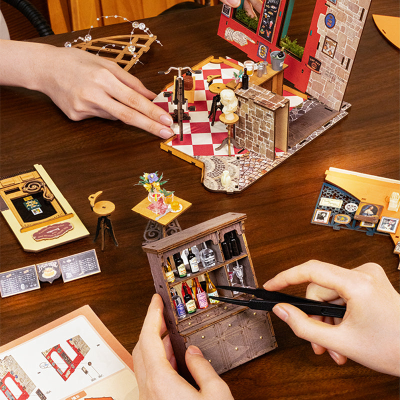 Miniature model setup on a wooden table with hands interacting with the models.
