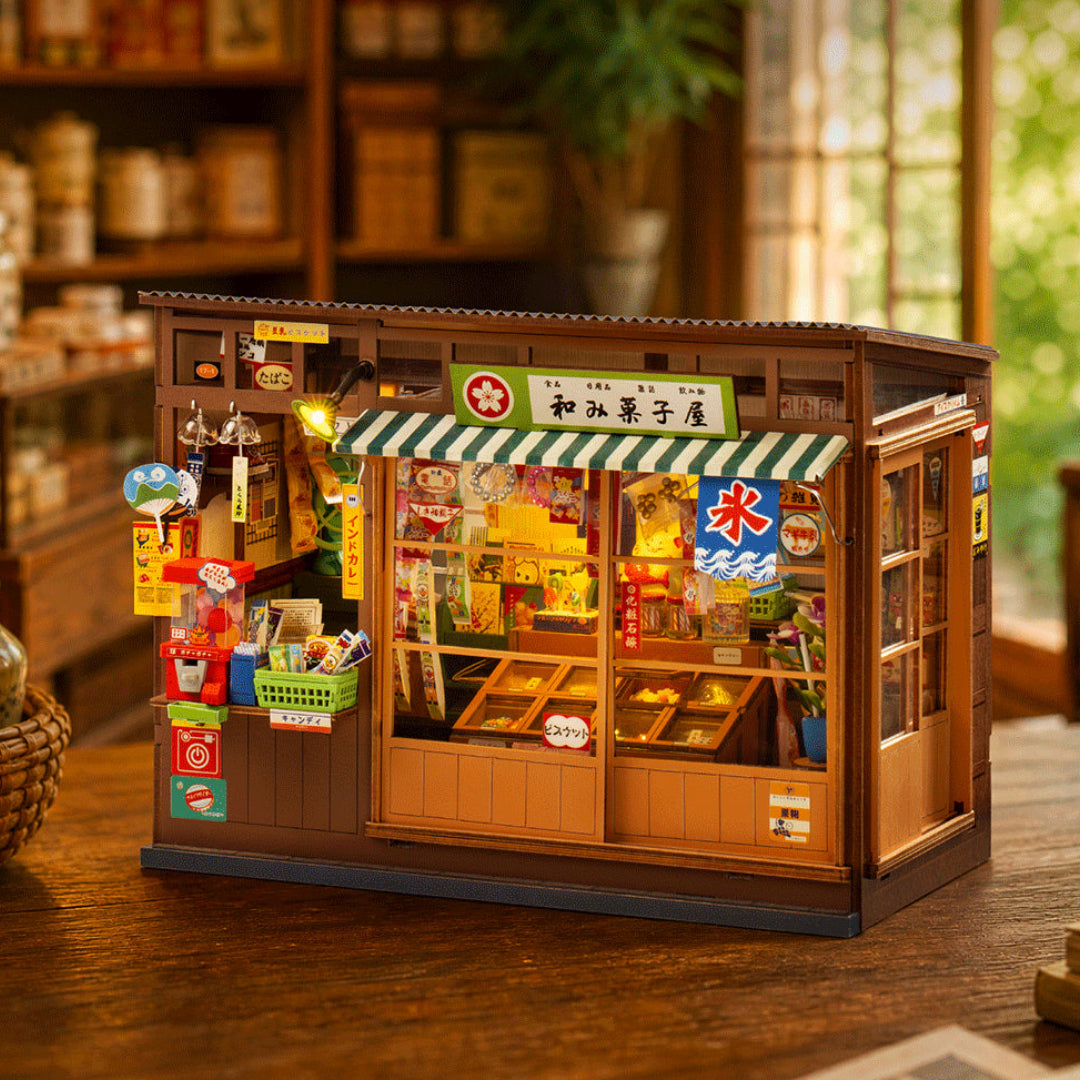 A miniature wooden toy shop model with detailed interior displays, Japanese signage, and colorful accessories, placed on a wooden table in a warm, blurred room setting.
