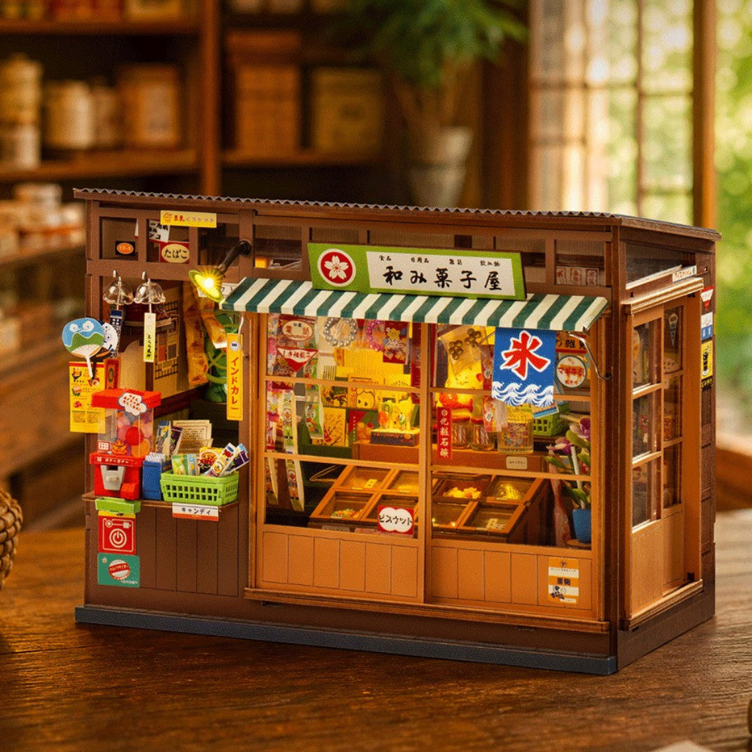A miniature wooden toy shop model with Japanese signage, detailed display windows, and colorful accessories, placed on a wooden table in a warm, blurred indoor setting.