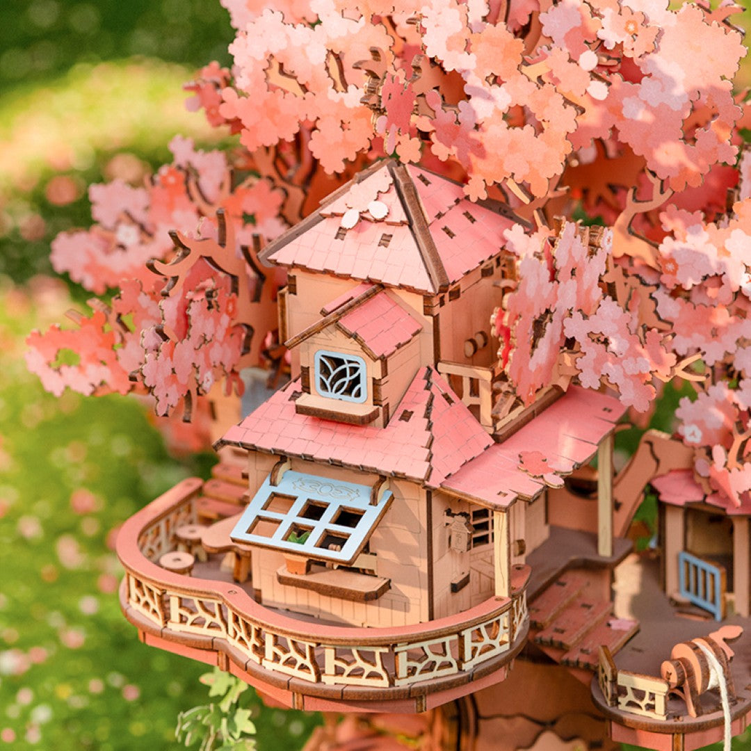 Wooden model of a treehouse with cherry blossom branches in a garden setting