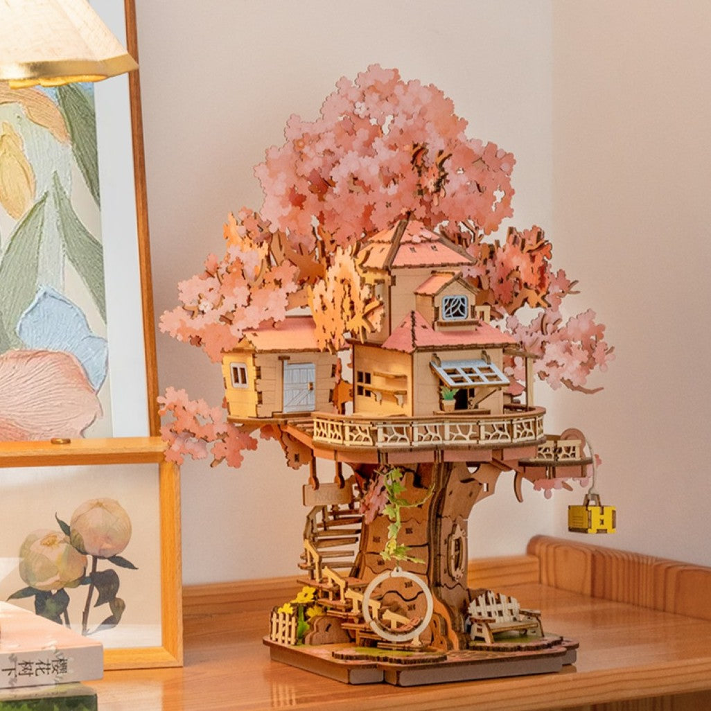 Wooden treehouse model with cherry blossom branches on a desk