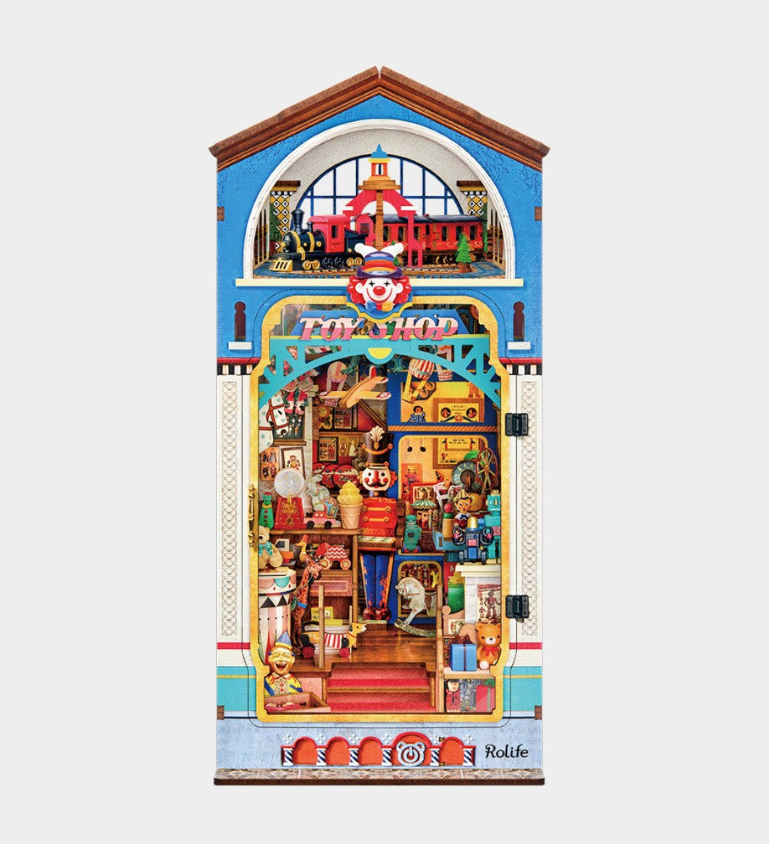 A colorful illustrated cabinet or display box shaped like a shop front, featuring a blue upper facade, arched window, and an open lower section filled with miniature toy-like objects and figures. The artwork is highly detailed and multicolored, shown centered on a plain light gray background.