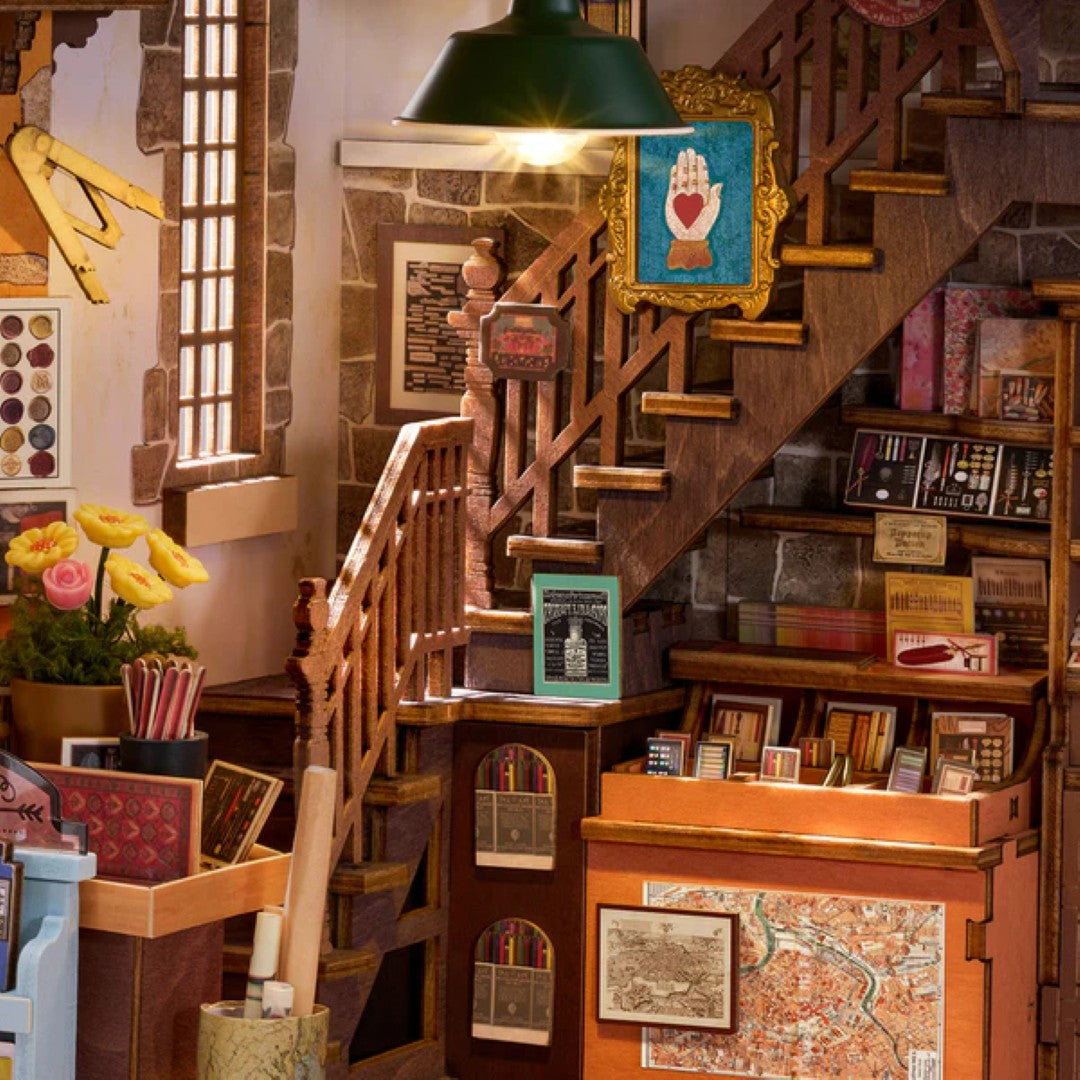 A miniature dollhouse-style interior scene with a wooden staircase, green dome ceiling lamp, stone walls, bookshelves, framed art, and decorative accessories.