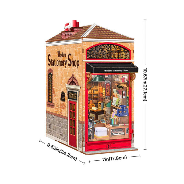 A miniature wooden stationery shop model shown with dimension lines and measurements on a plain white background. The shop features a warm beige brick exterior, a red door and awning, and a detailed interior visible through the large window.