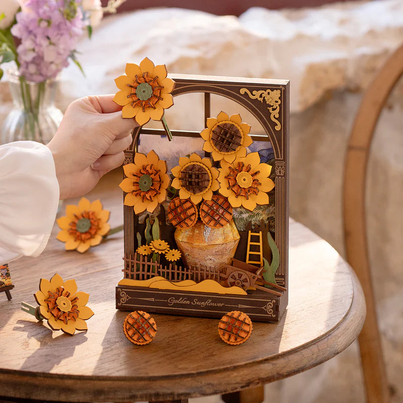 Decorative sunflower-themed shadow box on a wooden table with a hand holding a sunflower.