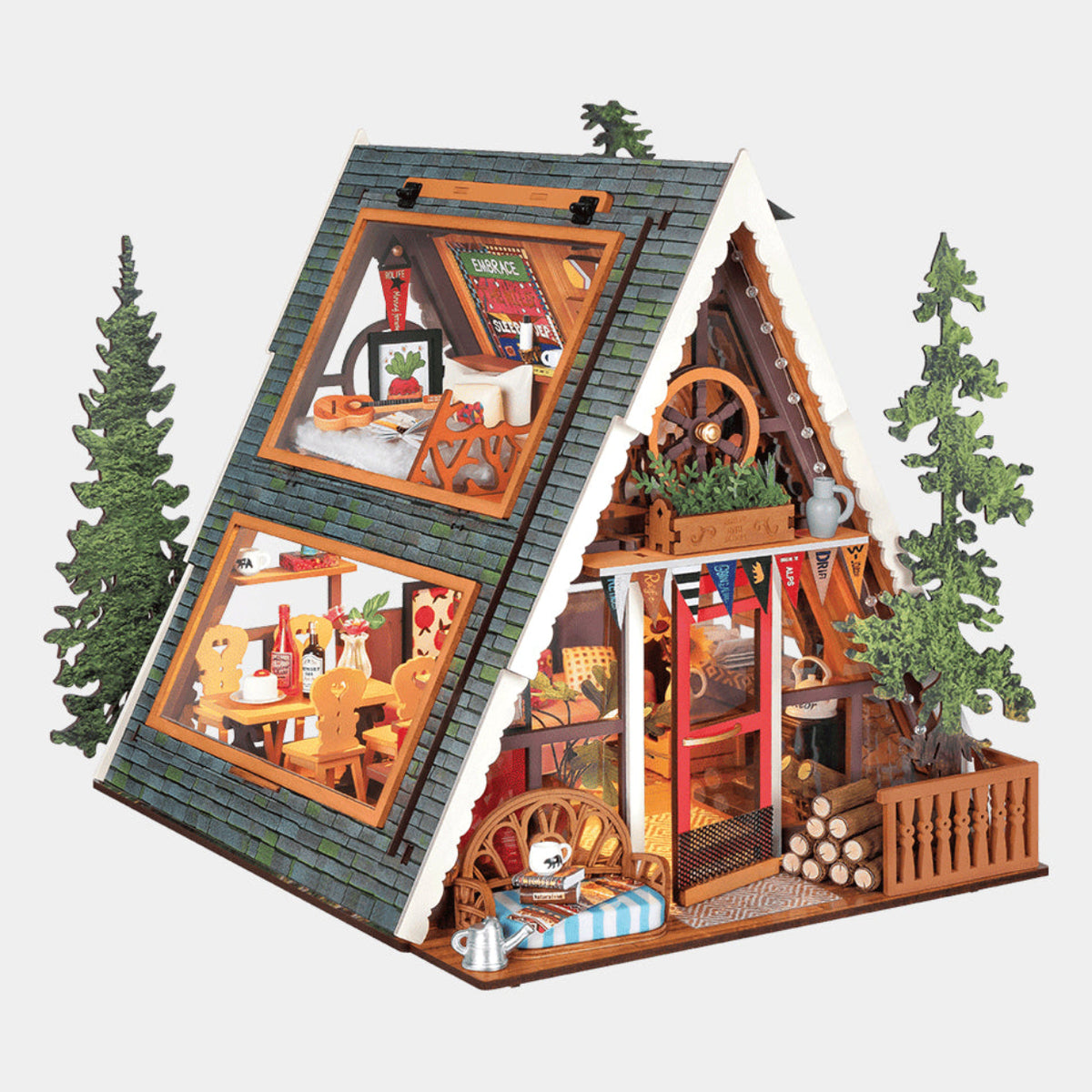 A detailed miniature A-frame cabin dollhouse with a gray shingled roof, warm wood-toned walls, and tiny furnished rooms visible through large windows, flanked by small green pine trees on a light gray background.