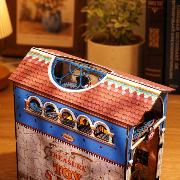 A 3D wooden model building kit shaped like a vintage treasure ship or house, featuring a brown scalloped roof, blue upper facade, and stone-textured lower section with 'Treasure Toy' lettering, shown on a wooden table in a warm indoor setting.